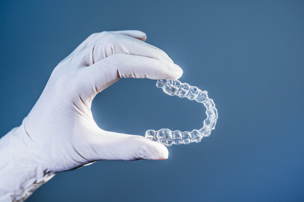Doctor hand holding a clear dental aligner with the blue background
